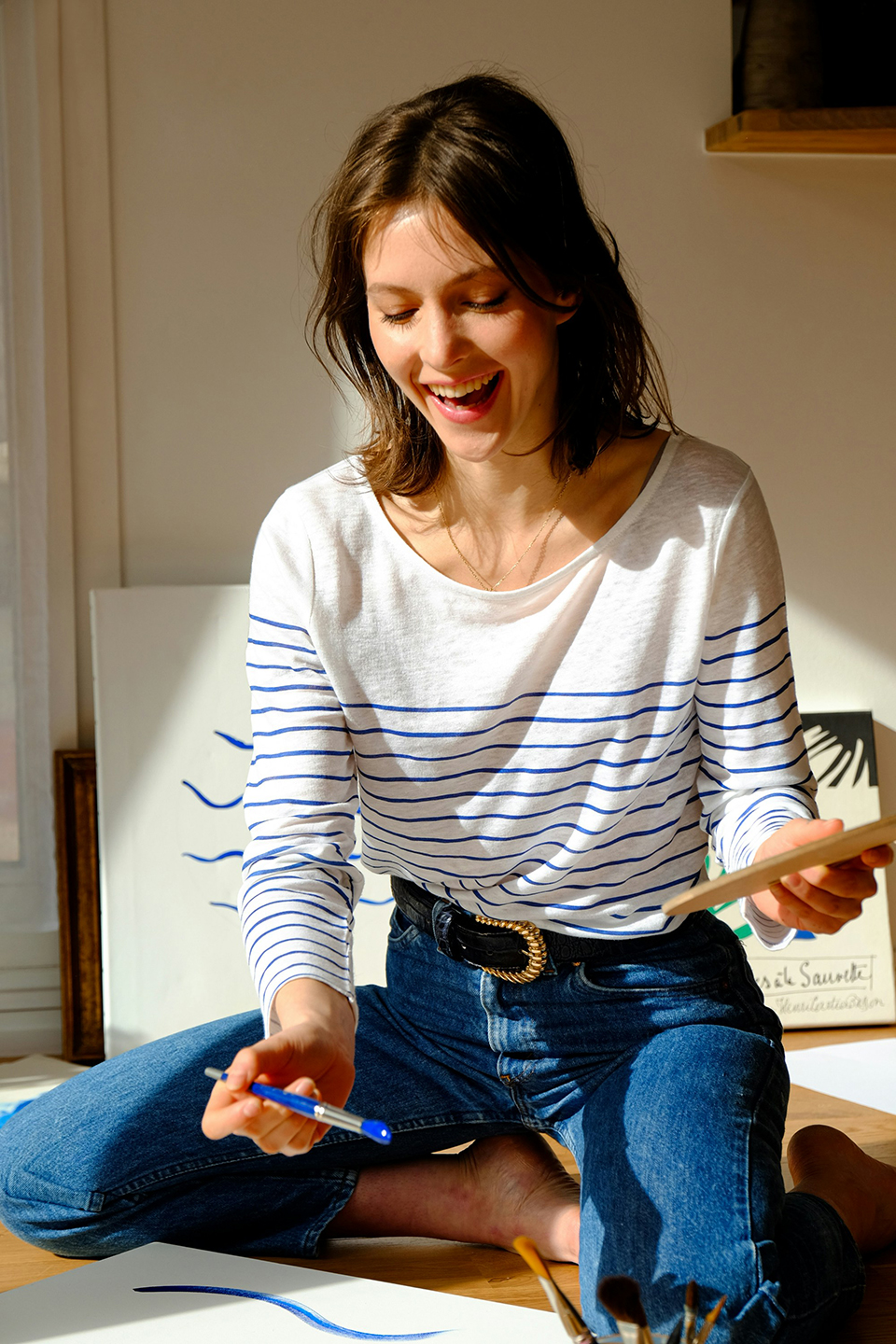 A smiling person sitting on the floor and writing on a tablet.